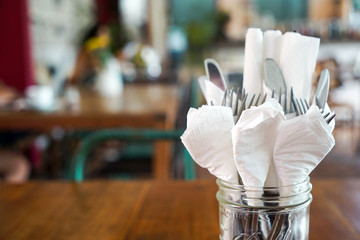 Cutlery (fork, knife, spoon) are wrapped in white napkins. Stand on a wooden table. Front view with copy space