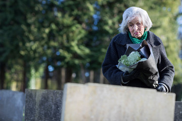 Sad Senior Woman With Flowers Standing By Grave