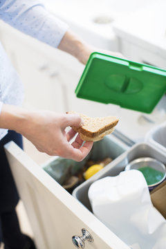 Close Of Woman Putting Food Waste Into Recycling Bin In Kitchen