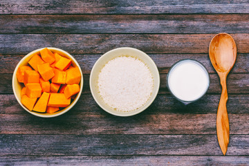ingredients for cooking pumpkin porridge. rice cereal, milk, slices of pumpkin and wooden spoon on a wooden grunge retro background, top view