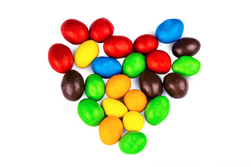 Multicolored candy dragees lined in the shape of heart on a white background