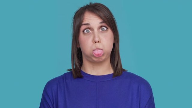 Portrait of hilarious female in casual making faces grimacing on camera  having fun being childish over blue background. Concept of emotions