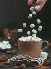 Keuken spatwand met foto Marshmallows falls from hand in glass mug with hot chocolate cocoa drink. Copy space. Winter food and drink concept. Flying marshmallow. Dark background. Low key. © fascinadora