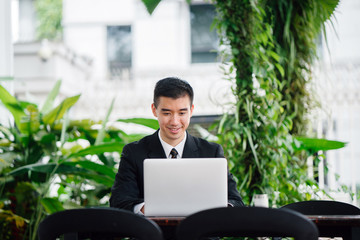 Portrait of young businessman wearing formal attire sitting at a cafe. He appears to be working on his laptop. 