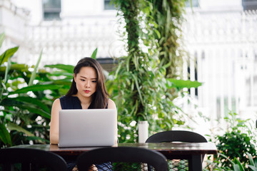 Portrait of young attractive businesswoman sitting and working at her laptop. She is looking at her screen and looks serious.