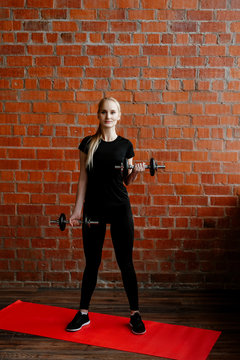 Portrait of beautiful blonde  woman in black sportswear standing against the background of  brick wall after fitness workout.Fites concept. The girl trains with dumbbells, does exercises on a biceps.