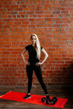 Portrait of beautiful blonde  woman in black sportswear standing against the background of a red brick wall after fitness workout.Fites concept. The girl does warm-up before a fitness training.