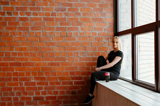 Portrait of beautiful blonde  woman in black sportswear standing against the background of a red brick wall after fitness workout.Fites concept. The girl poses, the place for copy spase nearby