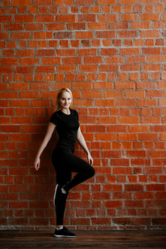 Portrait of beautiful blonde  woman in black sportswear standing against the background of a red brick wall after fitness workout.Fites concept. The girl poses, the place for copy spase nearby