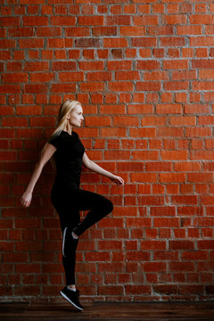 Portrait of beautiful blonde  woman in black sportswear standing against the background of a red brick wall after fitness workout.Fites concept. The girl poses, the place for copy spase nearby