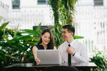 Portrait of a young professional colleagues sitting outdoors at a table. They have a laptop and appear to be smiling and discussing with one another. 