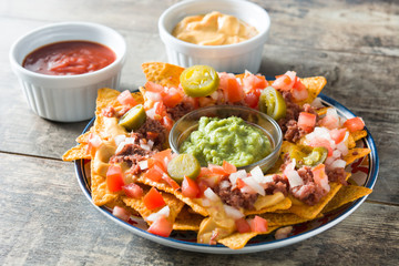 Mexican nachos with beef, guacamole, cheese sauce, peppers, tomato and onion in plate on wooden table