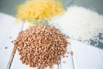 Diet, Organic Food, Vegetarian, Groats Concept. Piles of white rice, buckwheat and macaroni on a table in a close up, white wood and blue linen cloth as a background