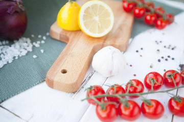 Diet, Healthy Food Cooking, Vegetarian Concept. Set of indredients: fresh cherry tomatoes, lemon on a cutting board, red onion, salt grains and black pepper corns on white wooden table
