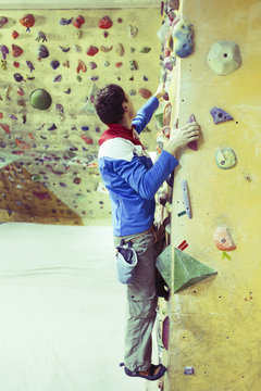 Young man practicing rock-climbing on a rock wall indoors.