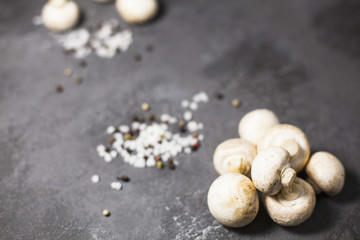 Diet, Italian Food Cooking, Vegetarian Concept. Fresh button mushrooms, sea salt grains and black pepper corns on a dark concrete background, selective focus