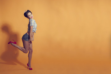 girl in pin-up style on a yellow background flexes leg