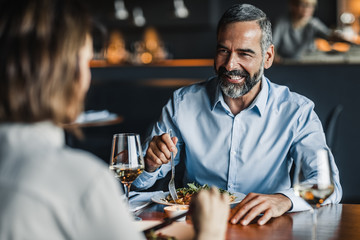 Handsome Caucasian middle-aged smiling man enjoying dinner at restaurant with a woman.