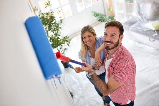 Young happy couple painting walls at new apartment