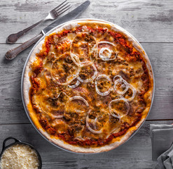 Pizza Bolognese served with onions, oregano and cheese on a rustic wooden table.