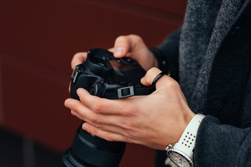 Close-up view of male hand holding professional camera outdoors. Dressed in warm jacket, white watches