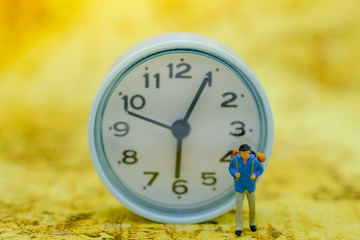 Travel and Time Concept. Traveller miniature figure with backpack walking on map with vintage round clock as backgroubnd