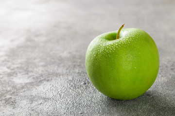 Juicy ripe green Apple with water drops on a concrete background. Selective focus and copy space