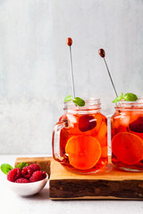 summer refreshing drink with ice and fresh ripe berries. raspberries and blackberries with citrus on a stone background table in glass jars with handles on a wooden serving board