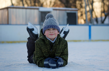 happy boy laying in skates on the ice rink