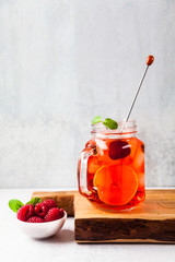 summer refreshing drink with ice and fresh ripe berries. raspberries and blackberries with citrus on a stone background table in glass jars with handles on a wooden serving board