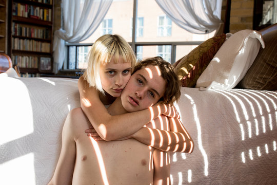 She embraces him from behind as they linger in bed