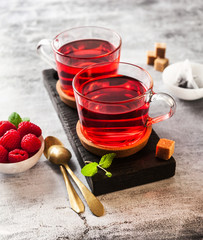 hot raspberry tea in two transparent cups on a stone table. Fresh berries, cubes of cane sugar and a bag of tea