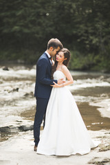 Fototapeta na wymiar Beautifull wedding couple kissing and embracing near the shore of a mountain river with stones