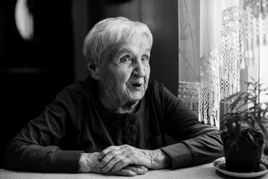 Elderly woman talking sitting at the table in the house. Black and white portrait.