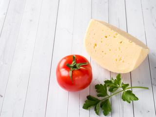 piece of cheese with parsley and tomato on white wooden background Copy space