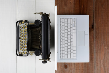 Overhead shot of and old fashioned typewriter back-to-back with a modern laptop computer on a white wood desk.