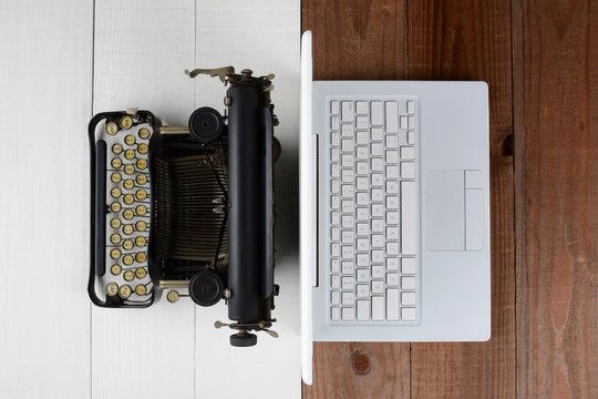 Overhead shot of and old fashioned typewriter back-to-back with a modern laptop computer on a white wood desk.