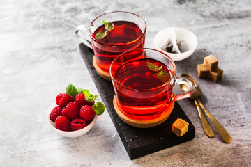 hot raspberry tea in two transparent cups on a stone table. Fresh berries, cubes of cane sugar and...