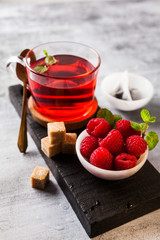 hot raspberry tea in transparent cup on a stone table. Fresh berries, cubes of cane sugar and a bag of tea