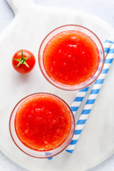 two glasses of freshly squeezed tomato juice on a marble serving board and cherry tomatoes. on a stone tableed tomato juice on a marble serving board and cherry tomatoes. on a stone table