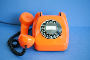 Busy retro phone orange color, handset receiver on blue background. Shallow depth field photography.