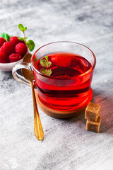 hot raspberry tea in transparent cup on a stone table. Fresh berries, cubes of cane sugar and a bag of tea