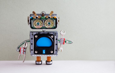 Fixing computer concept. Robotic handyman hand wrench pliers. Colorful display robot toy, empty blue monitor. Maintenance service works concept. Gray paper background, copy space.
