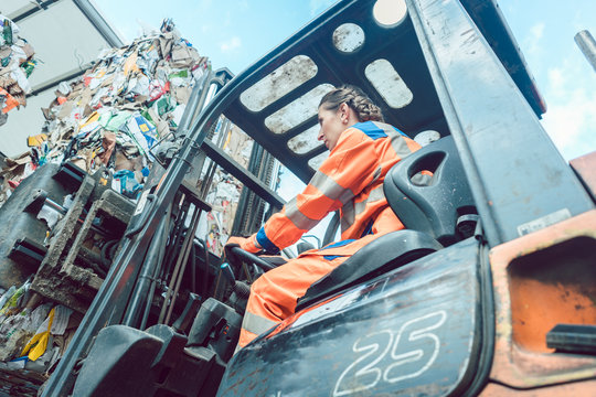 Female worker on forklift loading separated garbage on truck