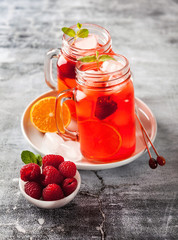 summer refreshing drink with ice and fresh ripe berries. raspberries and blackberries with citrus on a stone background table in glass jars with handles