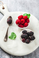fresh summer berries raspberries and blackberries with mint on a marble serving board in small marble bowls on a stone table. dessert serving of healthy food