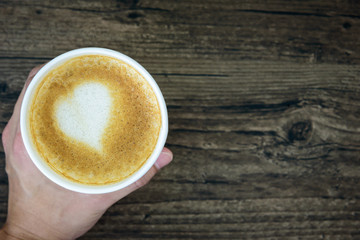 A man holding latte coffee with art heart milk isolated on brown wood table background. Flat lay with a cup of coffee valentine concept.