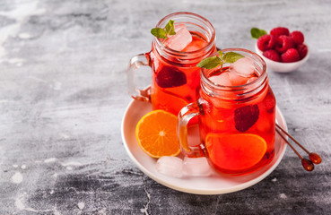summer refreshing drink with ice and fresh ripe berries. raspberries and blackberries with citrus on a stone background table in glass jars with handles