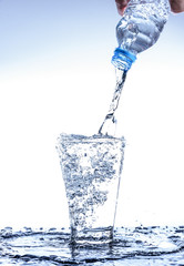 Pouring water and splashing in the glass with reflection on mirror.