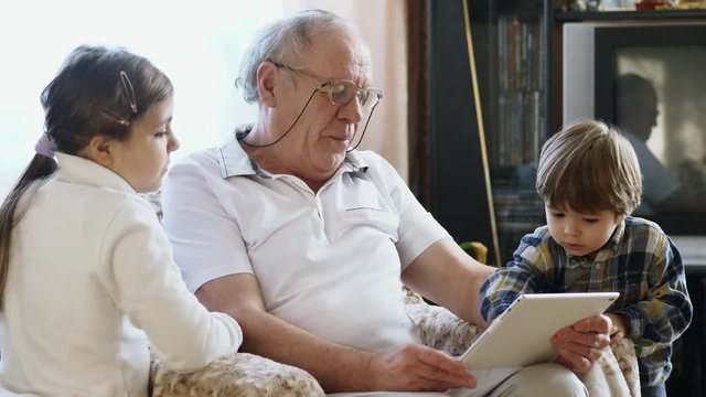 An elderly man using a tablet computer with grandchildren